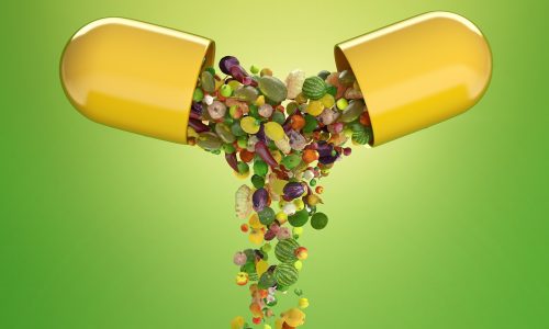 Vitamin Supplements A yellow capsule splits open, spilling out various small fruits and vegetables against a green gradient background. The image symbolizes the concept of vitamins or nutrients from natural food sources.