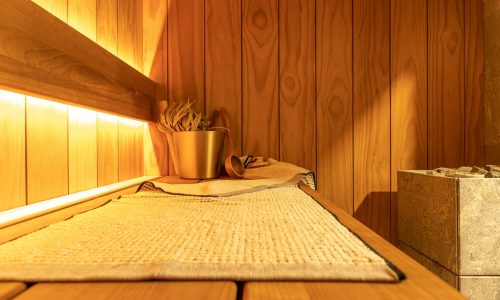 Interior,Of,A,Small,Modern,Sauna,For,One,Person,In A cozy sauna with wooden walls and benches, featuring a woven mat, a bucket with a ladle, and a bunch of sauna leaves. Warm, ambient lighting creates a relaxing atmosphere.